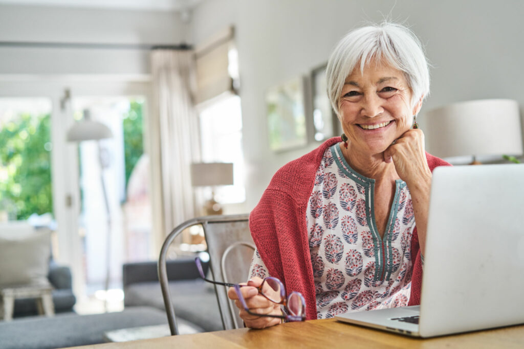 Portrait of a smiling senior woman sitting at a table at home and working on a laptop